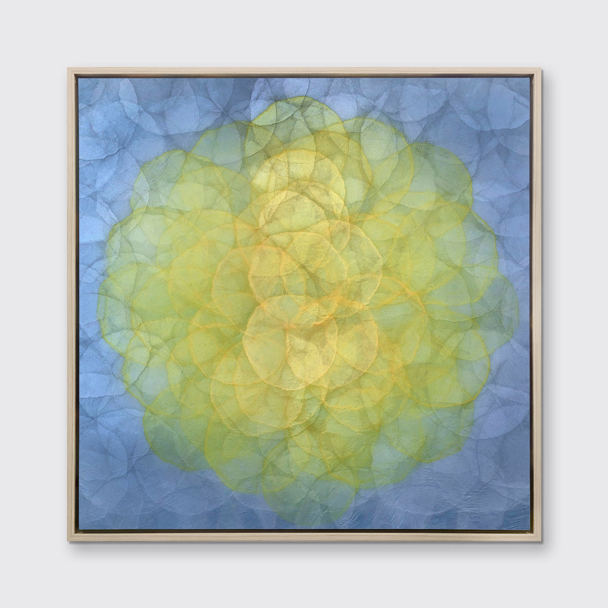 A blue and yellow abstract geometric print in a white oak wood floater frame hangs on a white wall.