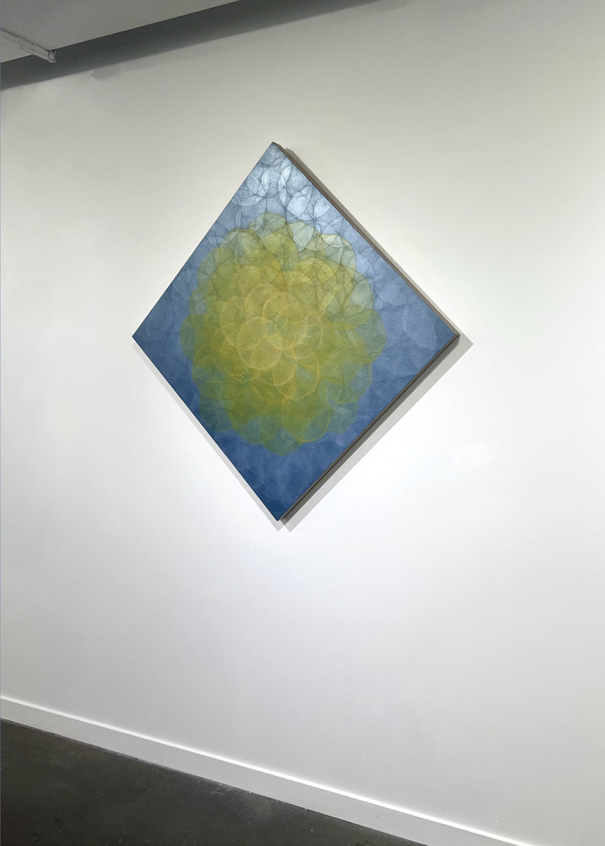 A blue and yellow abstract geometric painting hung on a white wall with a view from the right. 