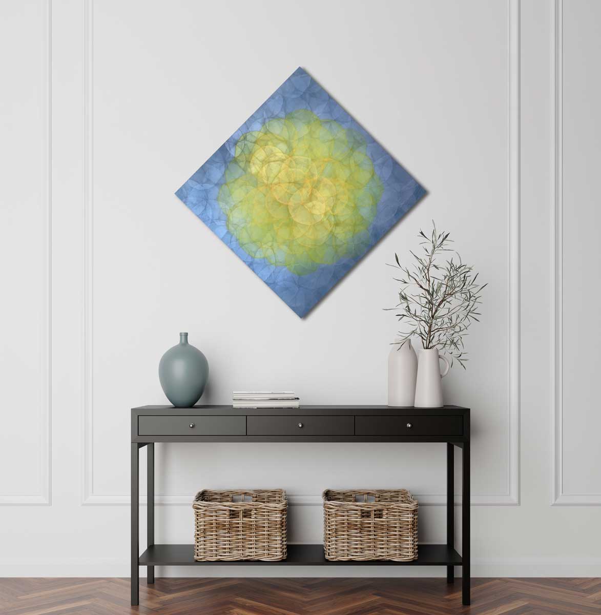 A blue and yellow abstract geometric painting hung on a white wall above a black console table. Atop of the table sits a blue vase, a stack of books, and two white ceramic vases with flowers. 