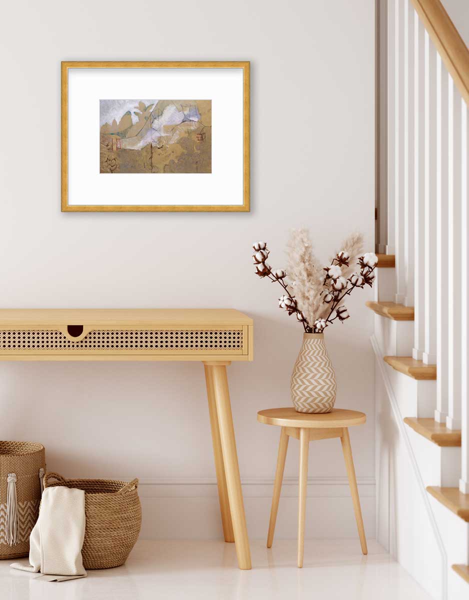 A dark gold and grey abstract print in a gold frame with a mat hangs on a white wall above a smooth wood desk, a two woven baskets and small side table with a vase with cotton stems.