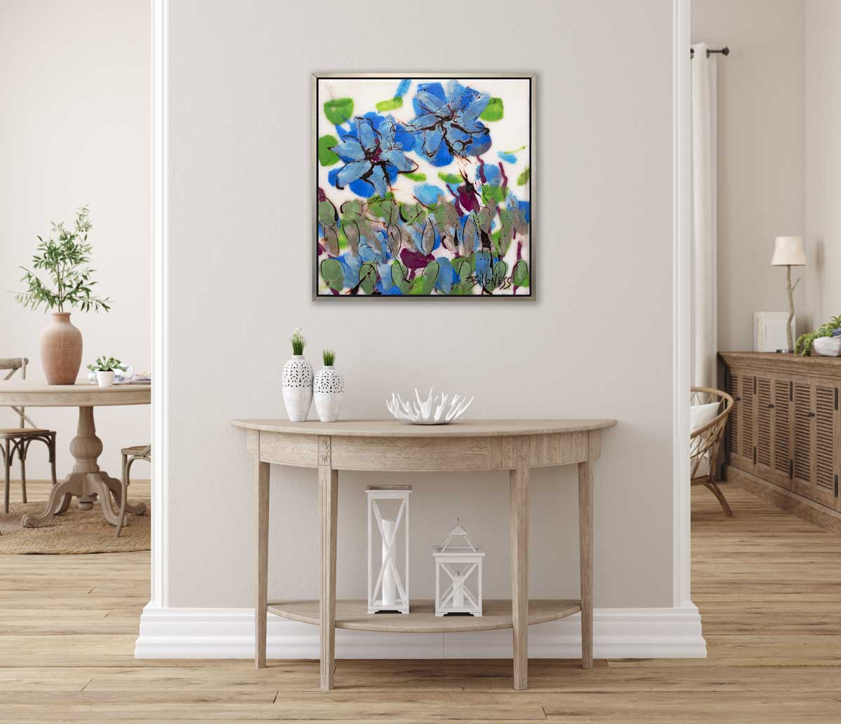 A blue, green and white abstract floral print in a silver floater frame hangs on a white wall above a natural wood half-circle console table with two white vases, a white decorative bowl and two white lanterns.