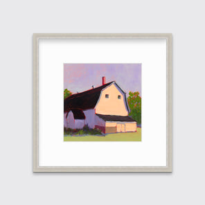 A print of a beige barn, a lavender sky, green bushes and trees and a light green foreground in a silver frame with a mat hangs on a white wall.
