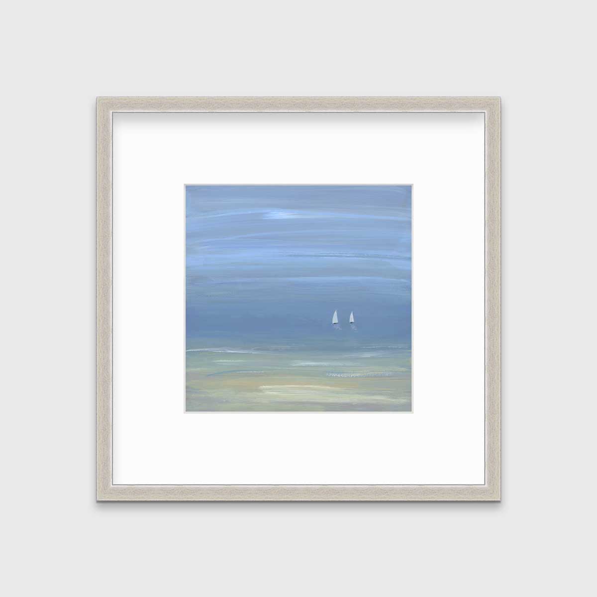 A blue, beige and white abstract seascape print with two small sailboats in a silver frame with a mat hangs on a white wall.