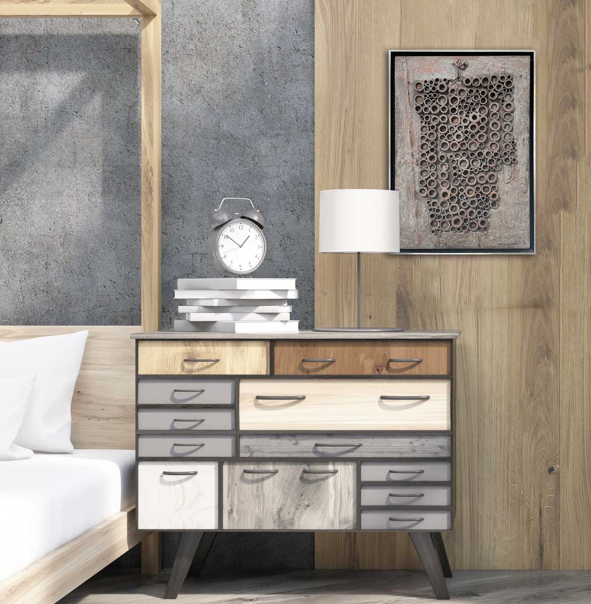 A grey abstract painting with embedded wood circles in a silver floater frame hangs on a wood plank wall above a wood dresser with a stack of books and a white table lamp.