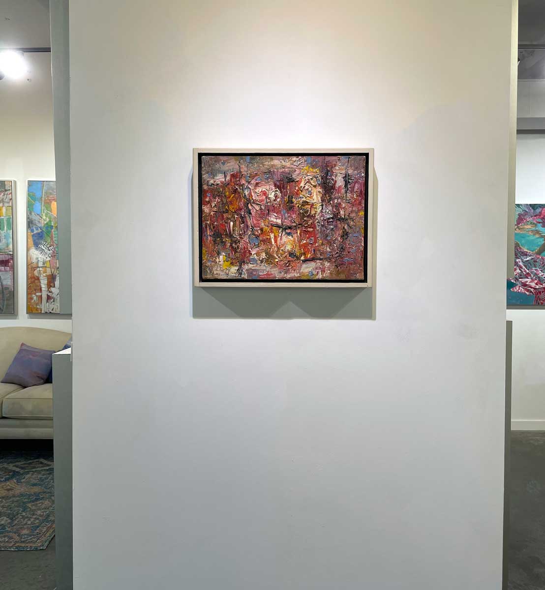 A multicolored abstract painting in a white floater frame hangs on a white wall.
