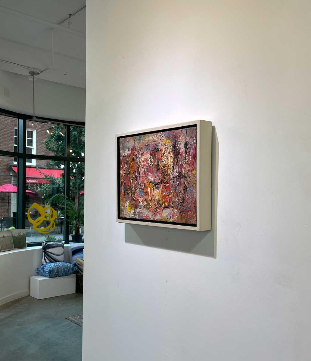 A right side-angle view of a multicolored abstract painting in a white floater frame hangs on a white wall.