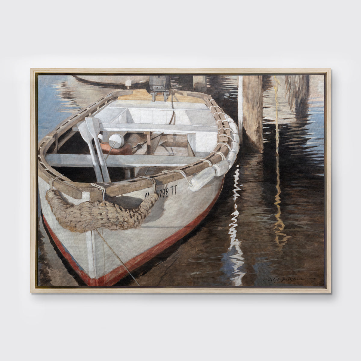 A print of a white and tan row boat at a dock in a white oak wood floater frame hangs on a white wall.