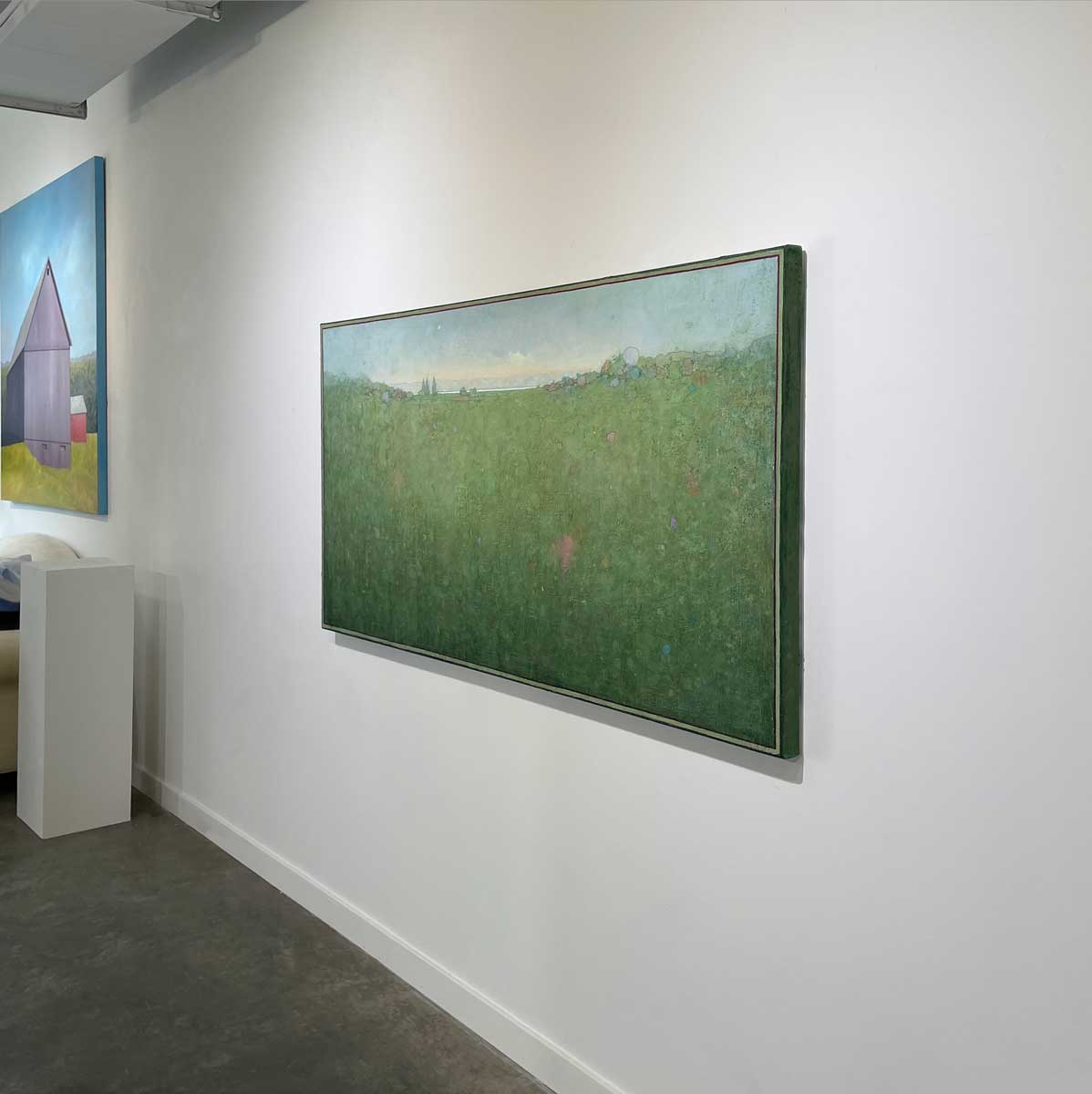 A right side-angle view of a green and blue abstract landscape painting by Elwood Howell hangs on a white wall.
