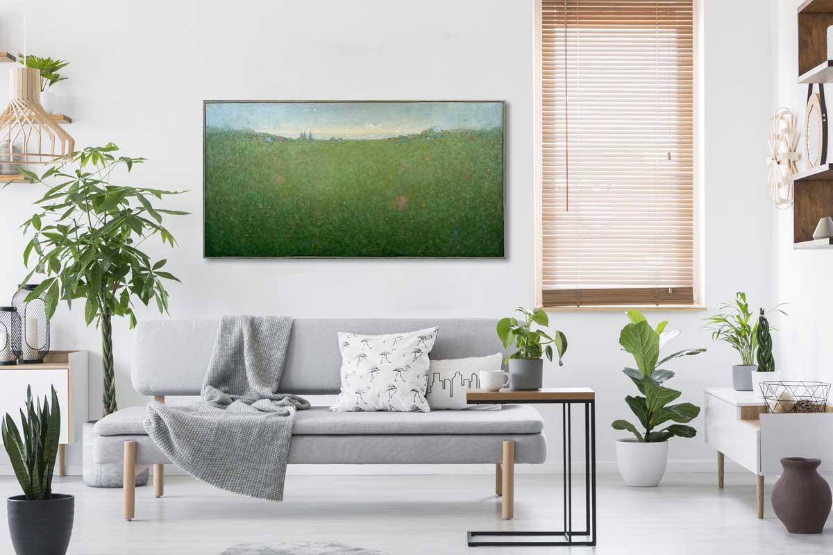 A green and blue abstract landscape hangs on a white wall above and behind a grey modern sofa with pillows and several potted plants all over.