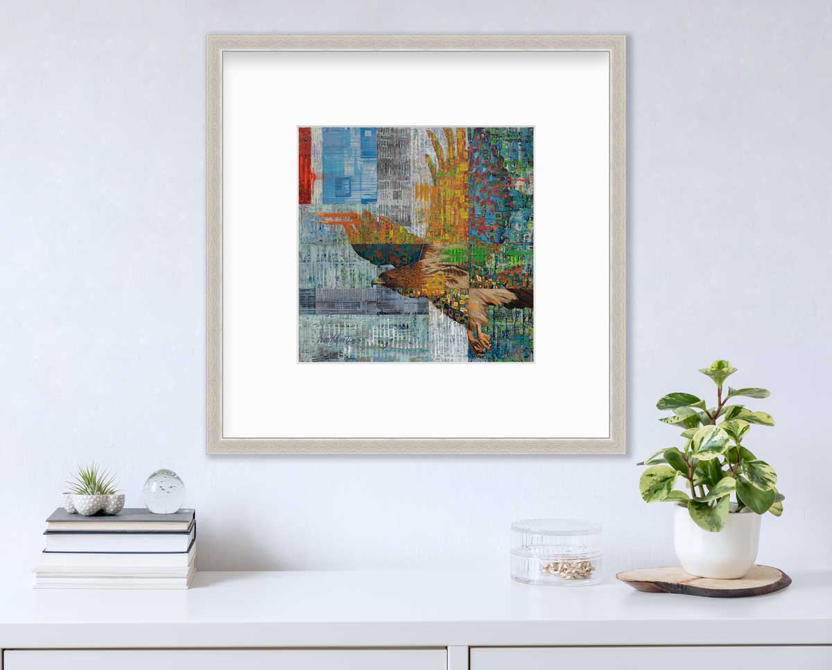 A multicolored abstract print of a flying eagle in a silver frame with a mat hangs on a white wall above a white surface with a stack of books, a clear round container with gold accessories and a potted plant.