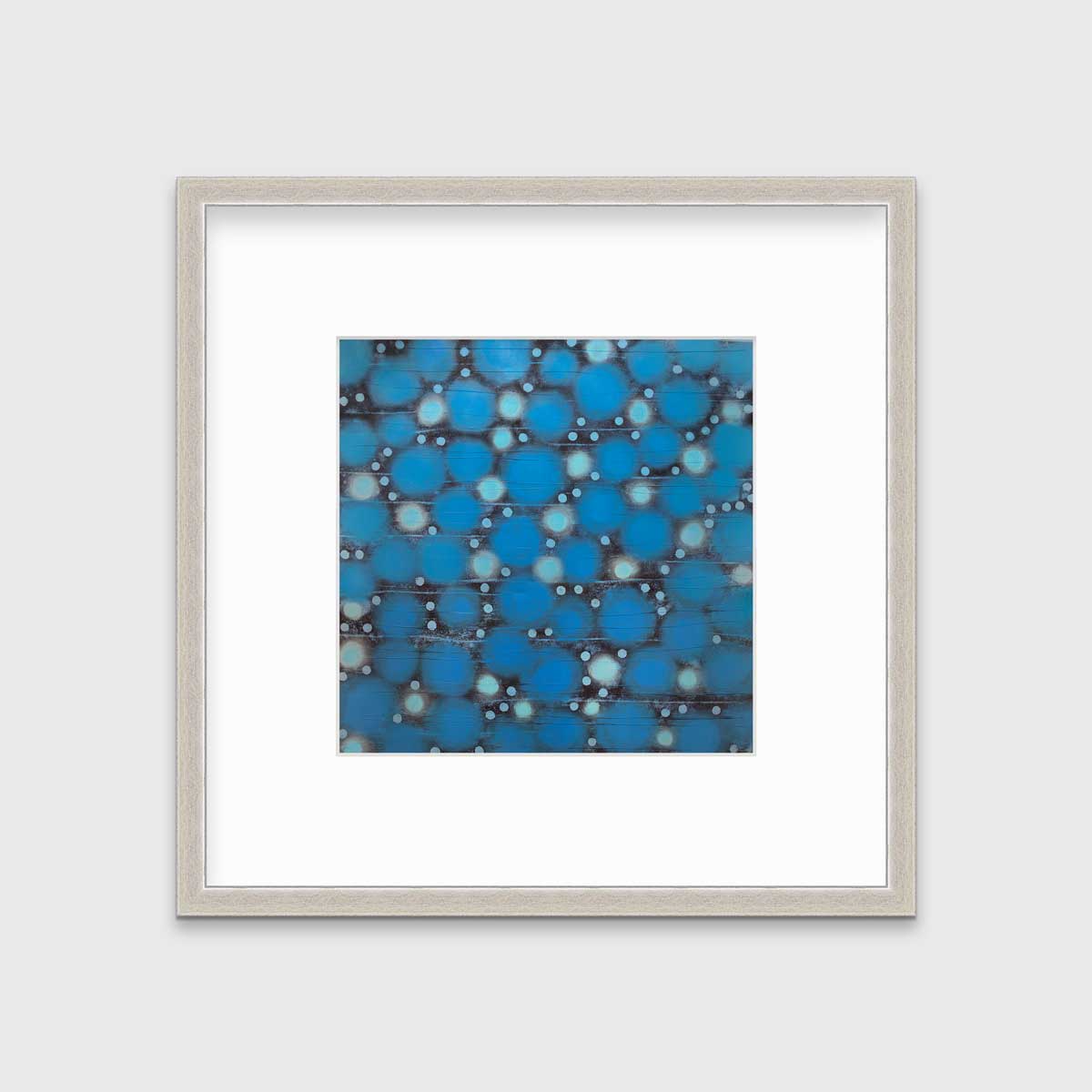 A blue, teal and black abstract circle print in a silver frame with a mat hangs on a white wall.