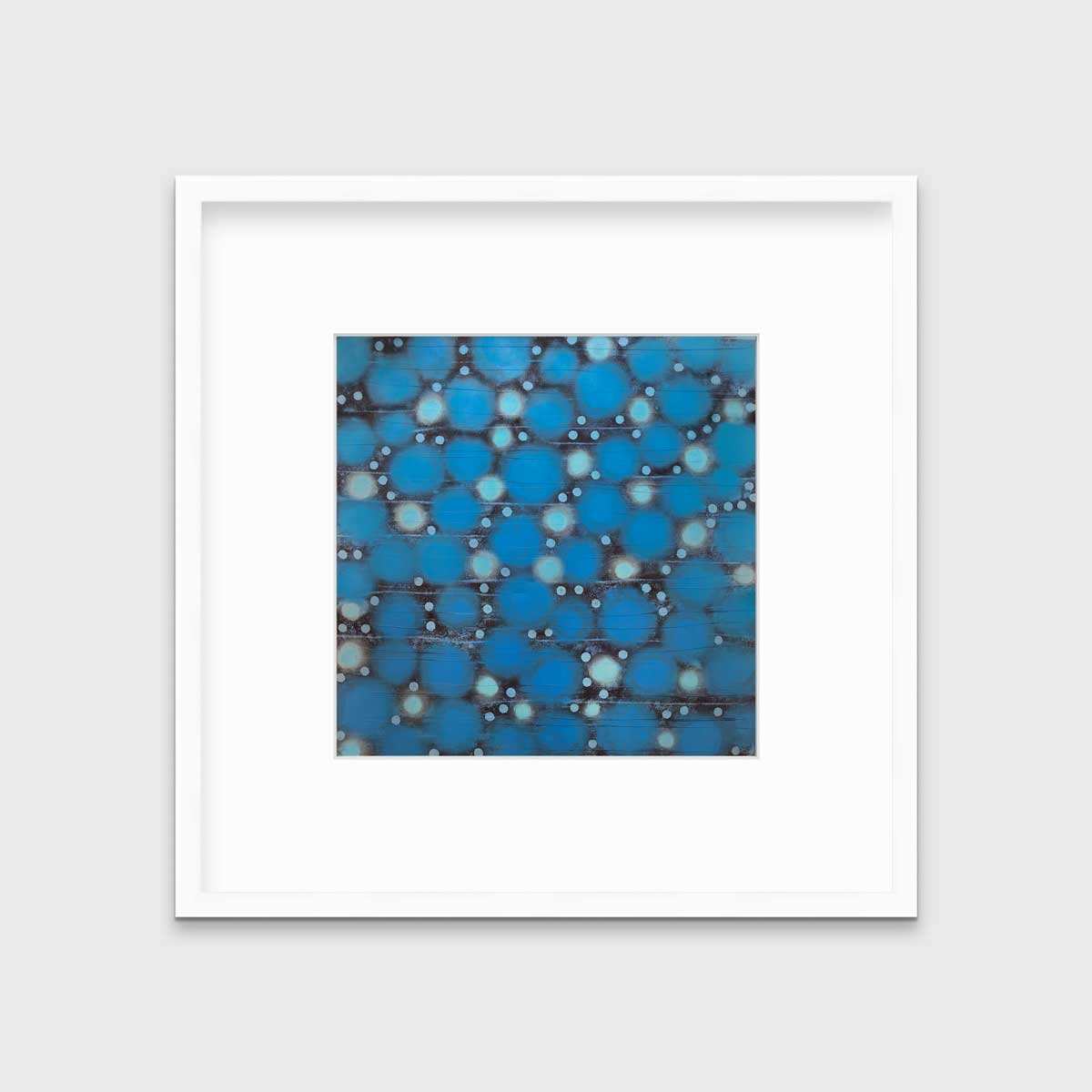A blue, teal and black abstract circle print in a white frame with a mat hangs on a white wall.