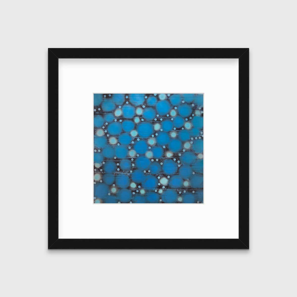 A blue, teal and black abstract circle print in a black frame with a mat hangs on a white wall.