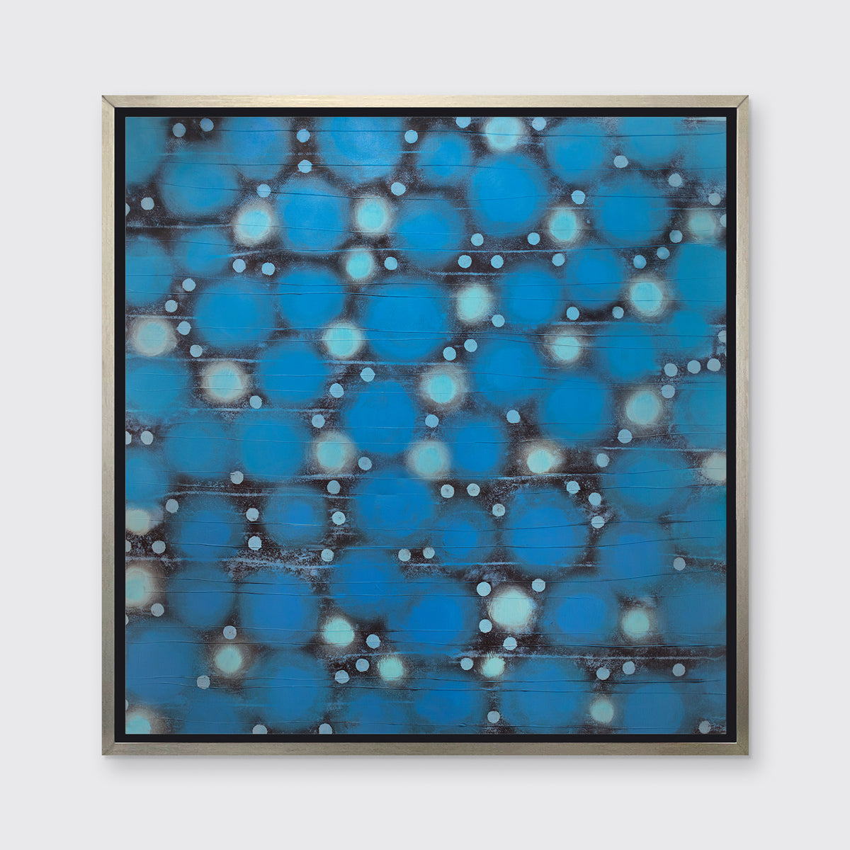 A blue, teal and black abstract circle print in a silver floater frame hangs on a white wall.
