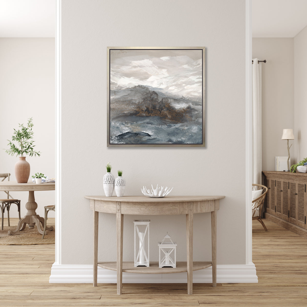 A beige, white, brown and grey abstract print in a silver floater frame hangs on a light grey wall above a wood half circle console table with two white vases, a decorative white bowl and two white lanterns.