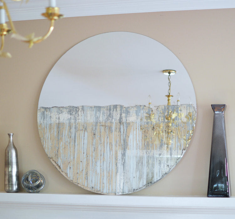 Circular mirror with grey mixed media painting on lower half. Displayed on the mantle, leaning up against the wall. Vases sit to the left and right of the mirror.