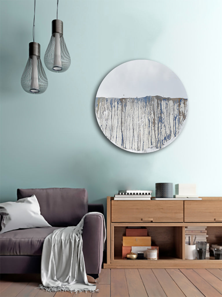 Circular mirror, mounted on wall, with blue and gold mixed media painting on lower half. Displayed in living room above a console with lounge chair to the bottom left.