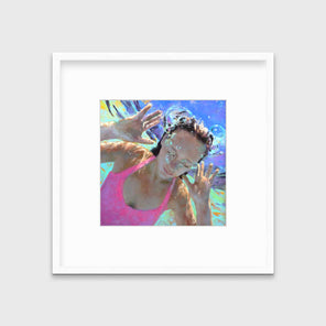 An abstract figurative print of a girl underwater in a pink swimsuit in a white frame with a mat hangs on a white wall.