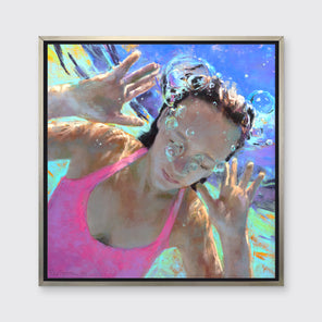 An abstract figurative print of a girl in a pink swimsuit underwater, hangs on a white wall in a silver floater frame.