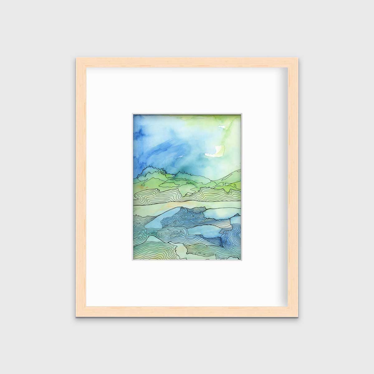 A green and blue abstract landscape illustration print in a natural wood frame with a mat hangs on a white wall.