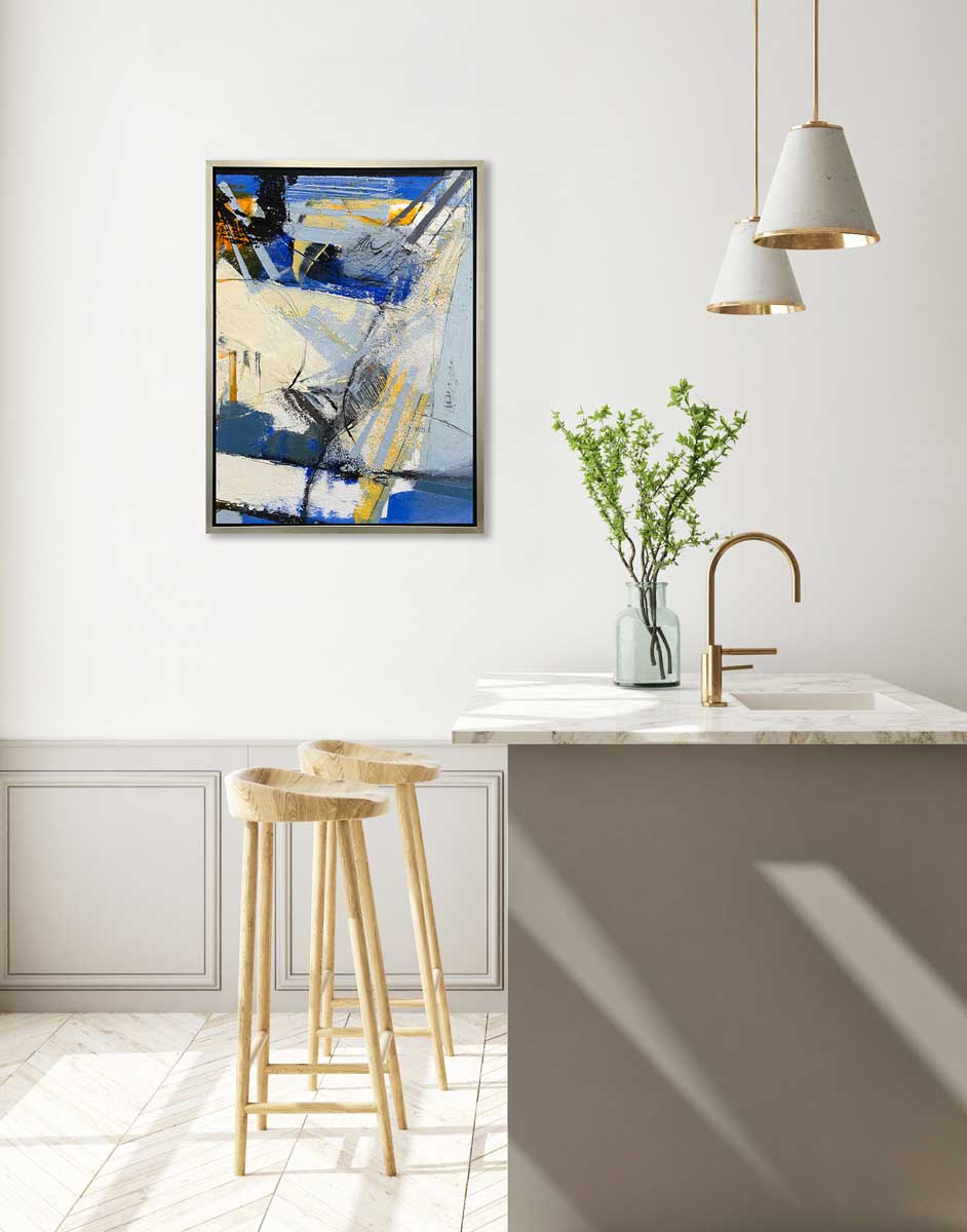 A blue, white, yellow and black abstract print in a silver floater frame hangs on a white wall above a white marble kitchen island with a sink and a clear bottle with floral stems and two wood counter stools.
