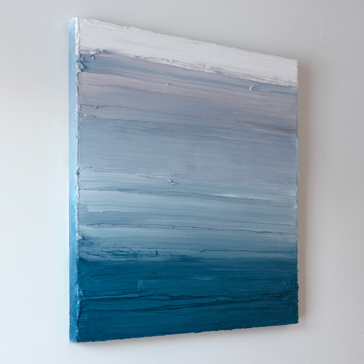A left side-view of a white, light grey and tonal blue abstract painting by Teodora Guererra hangs on a white wall.