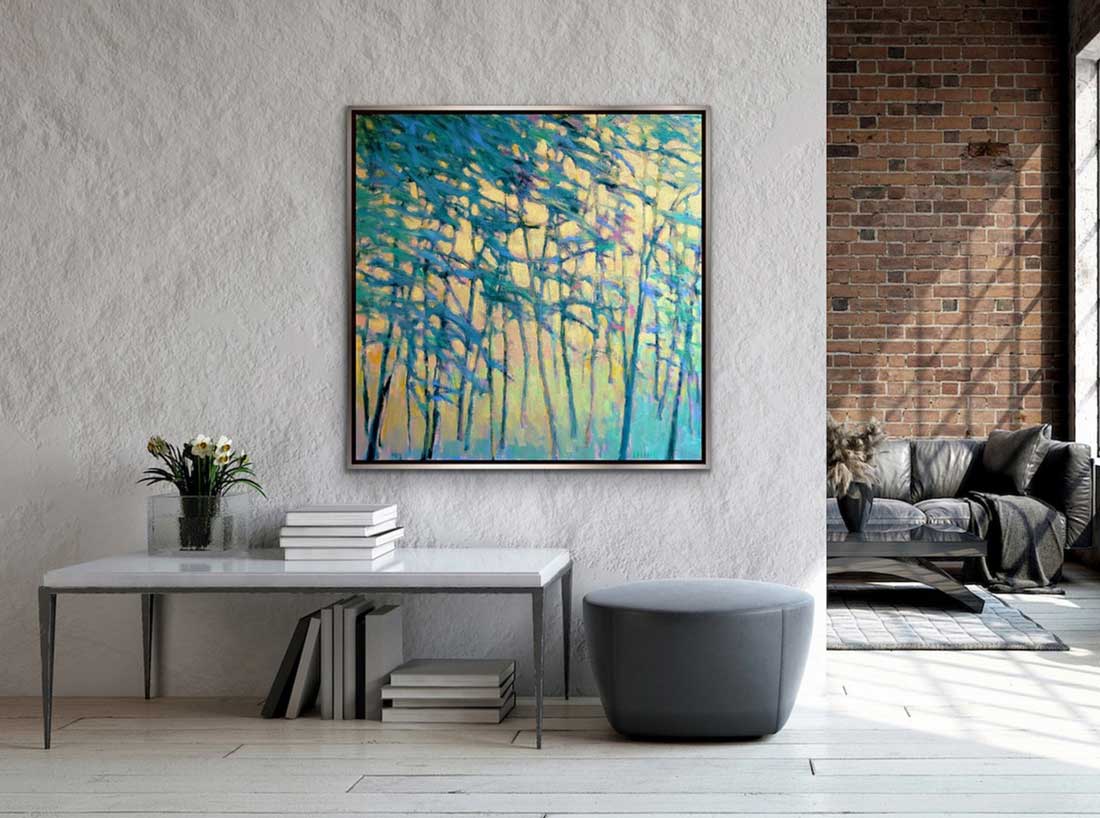 The painting, Air Through the Forest by Ken Elliott hanging on a white wall in a warm silver floater frame above a white table and grey ottoman.