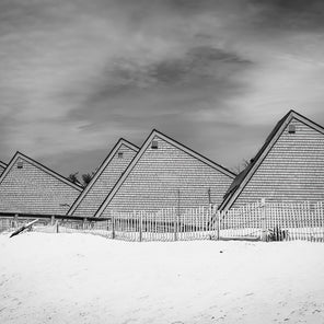 A black and white photograph of triangular-shaped houses on a sandy beach. 