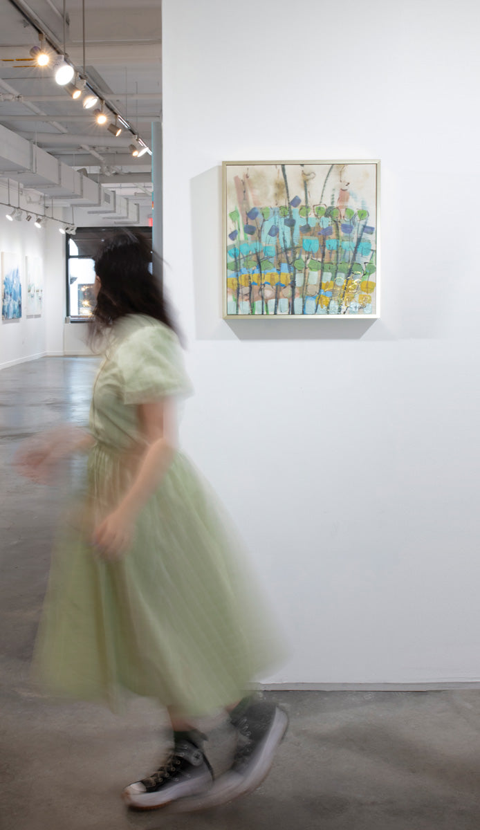 A woman wearing a green dress walks by an abstract painting by Linda Bigness which hangs on a white wall. 