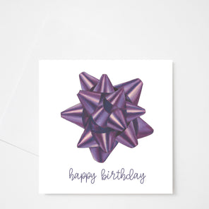 A white greeting card with a purple bow in the center with happy birthday text in purple at the bottom displayed above a white envelope on a white background. 