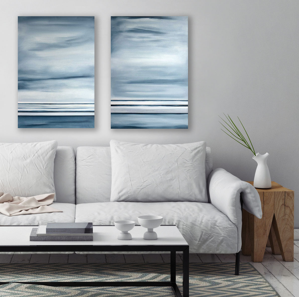Two blue-grey abstract paintings hang on a light-grey wall above a white couch and minimalist coffee table. 