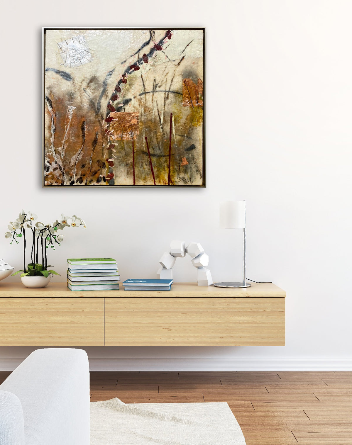A nature-inspired abstract painting, framed in a warm silver floater frame hangs on a white wall above a wooden console table. 