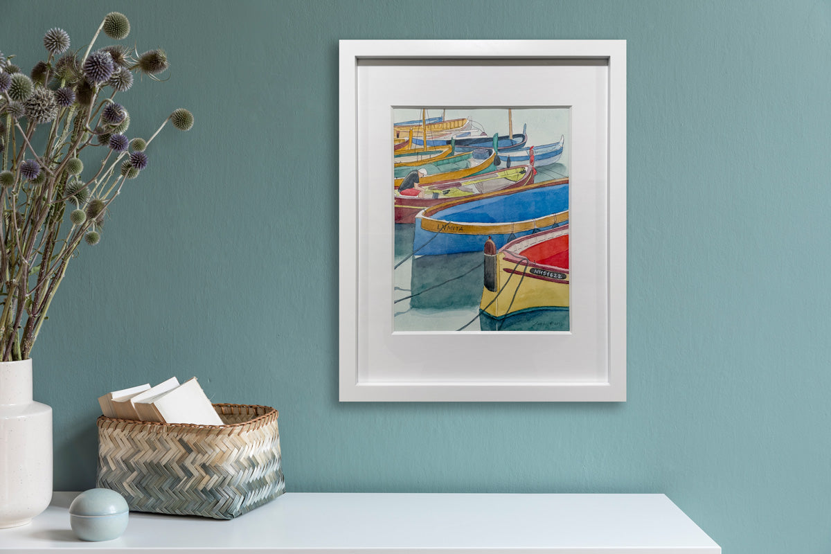 A colorful painting of boats in a white frame hangs on a teal wall above a white table with minimalist decor. 