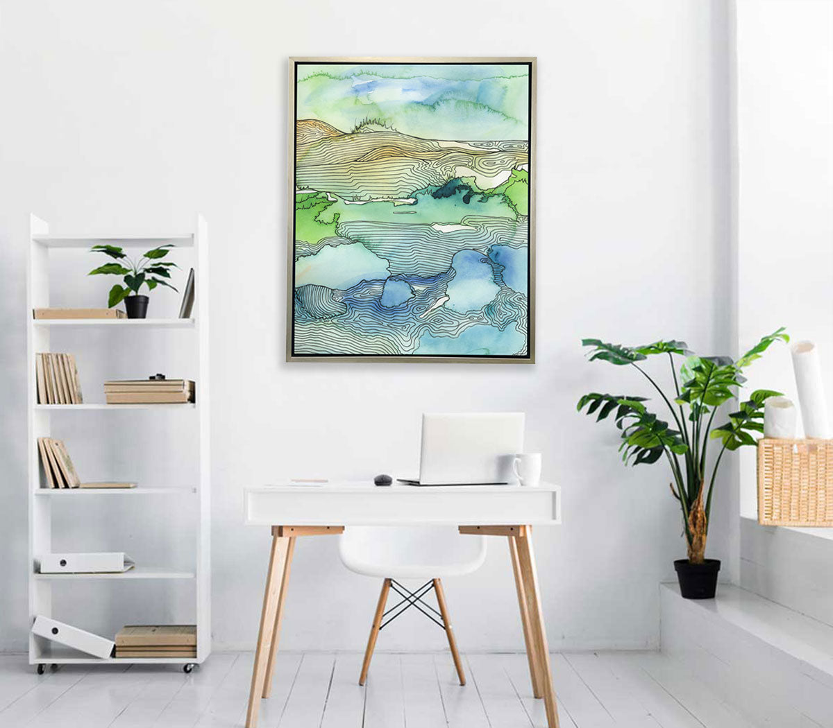 A blue and green landscape illustration print hangs on a white wall above a small modern white desk, a book shelf, and potted plant. 