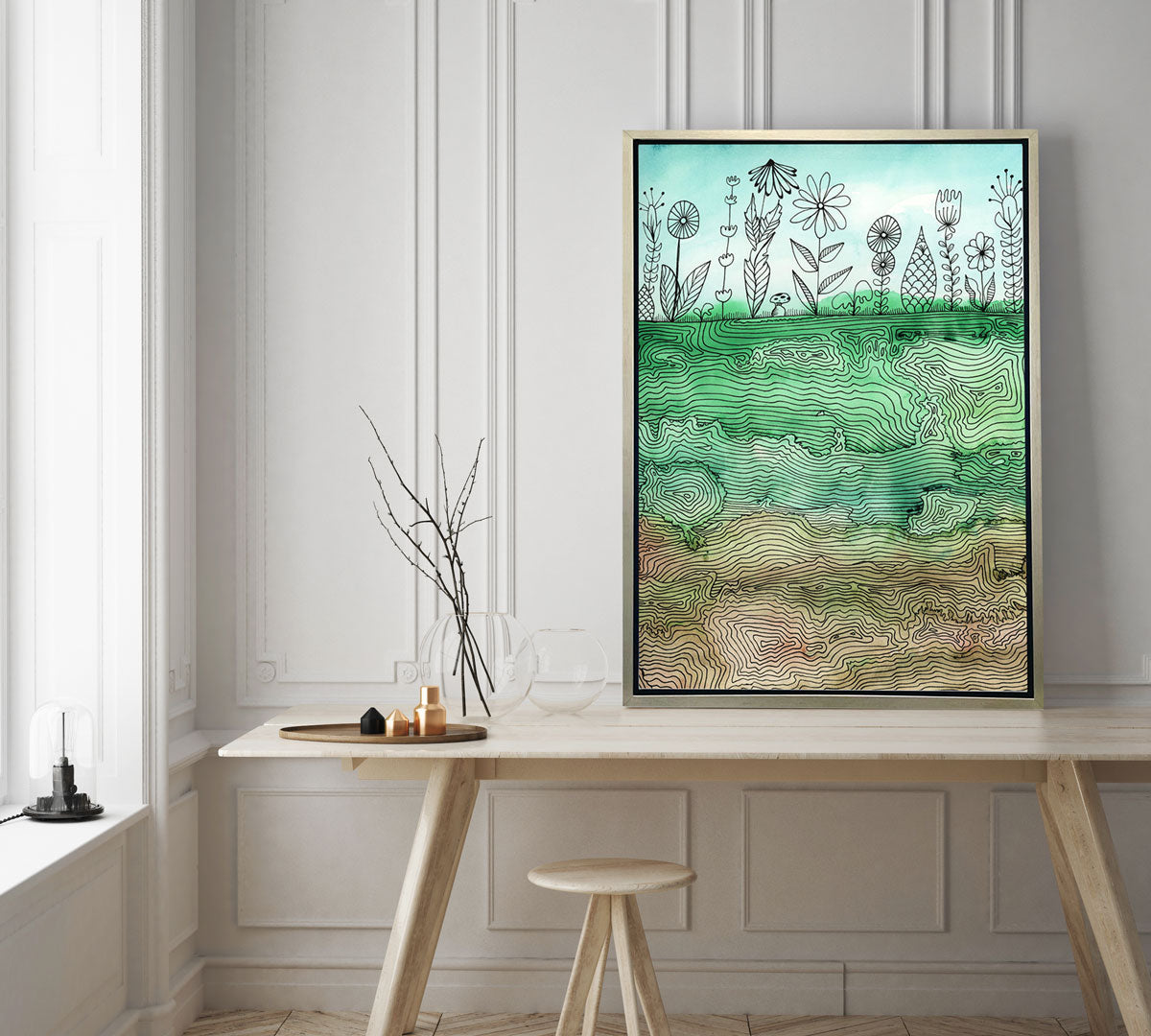 An illustration canvas print rests on a minimalist wooden desk against a paneled white wall. 