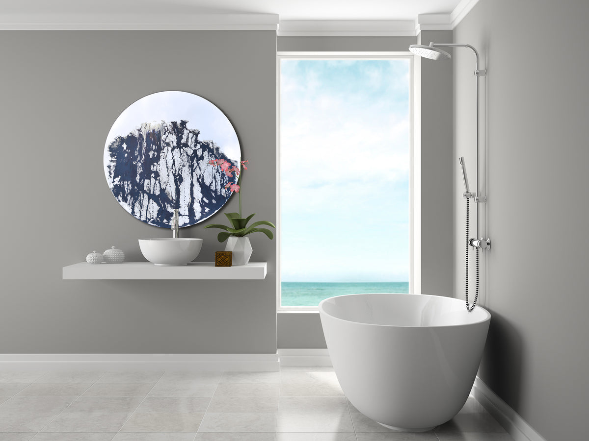 Circular mirror with abstract, mixed media painting covering a majority of the surface. Mirror is mounted on the wall, to the left, in the bathroom above the sink. On the right is a bathtub that overlooks the ocean.   
