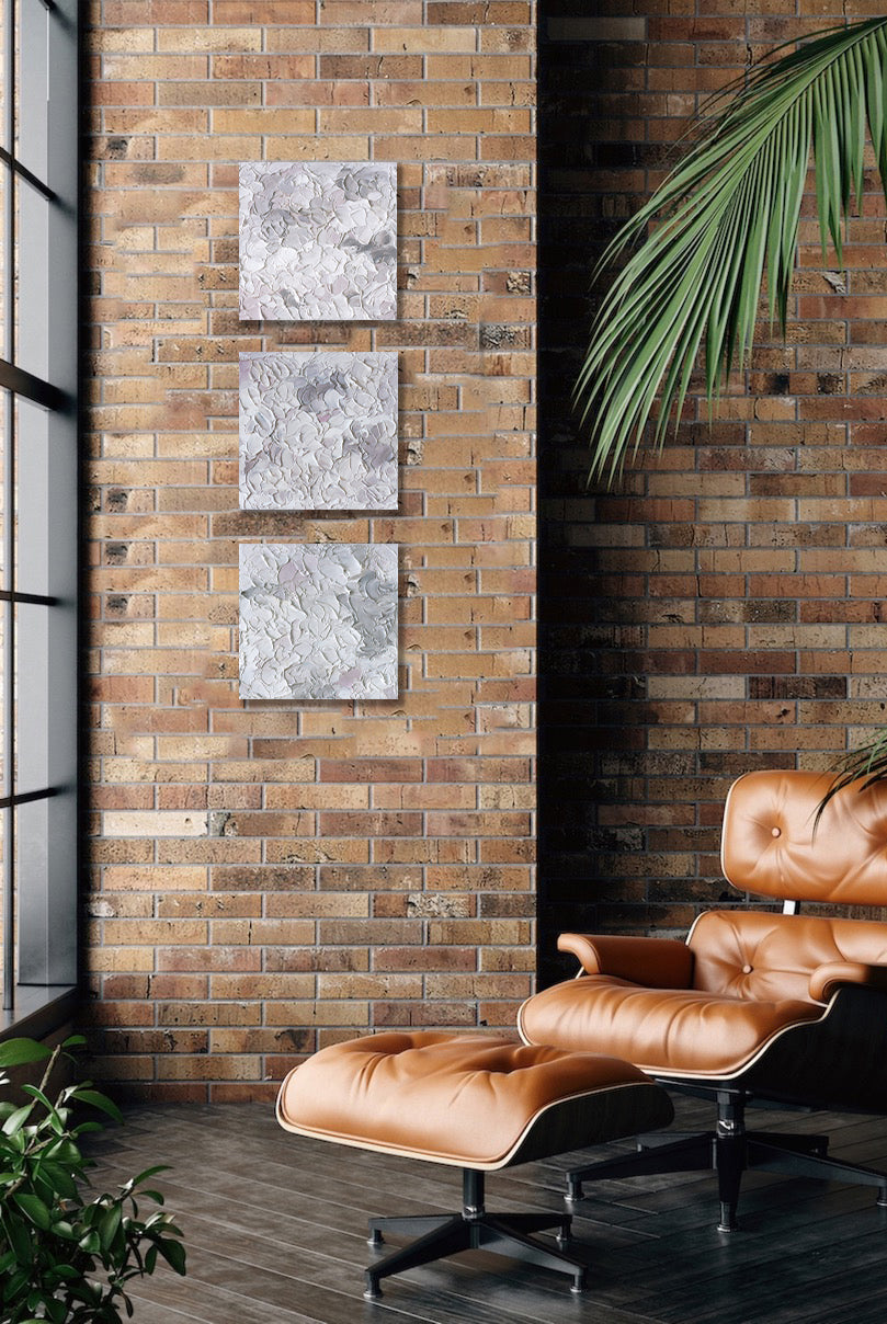 Three abstract painting by Teodora Guererra hang on a brick wall with a leather chair