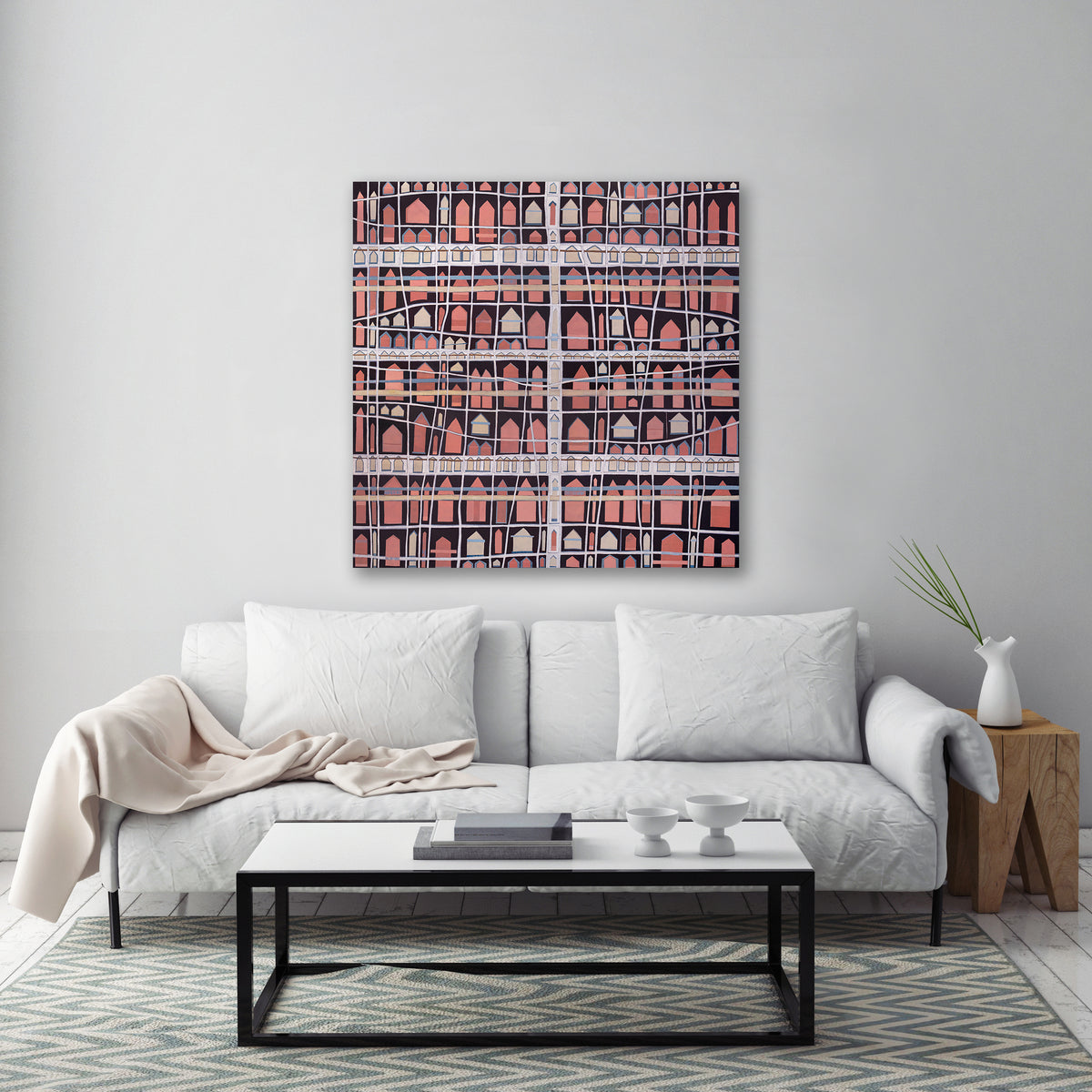 An abstract painting with cross hatching brushstrokes over small pink house shapes is hung over a white sofa.