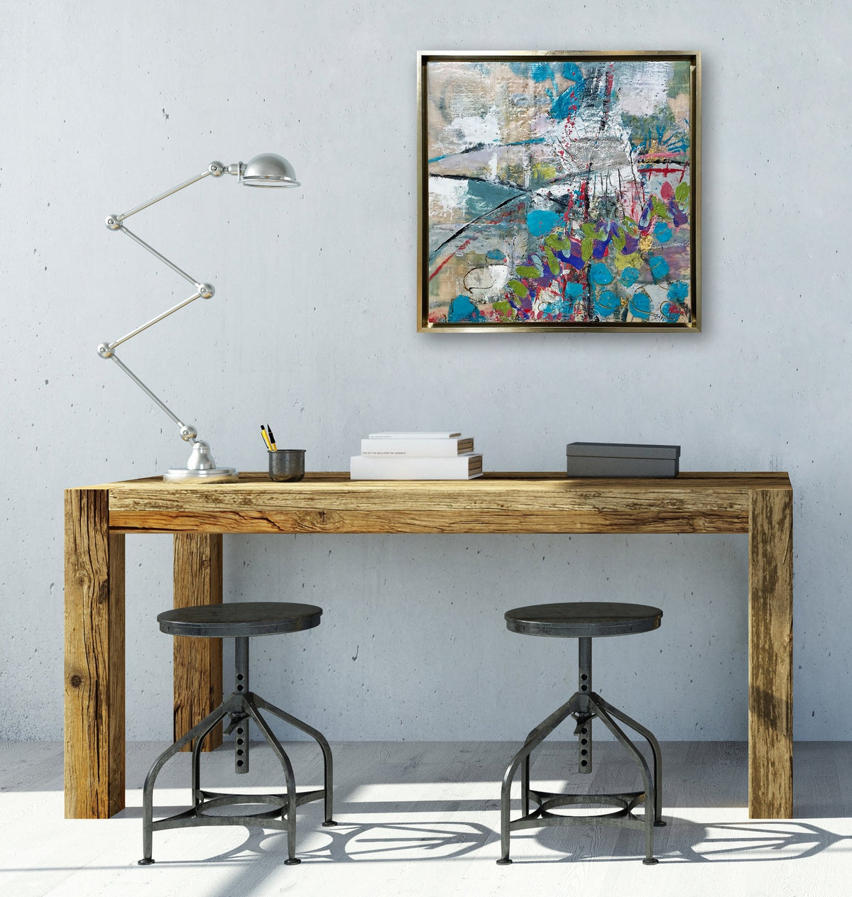 An abstract encaustic painting hangs in a gold frame above a simple wooden desk and black stools. 