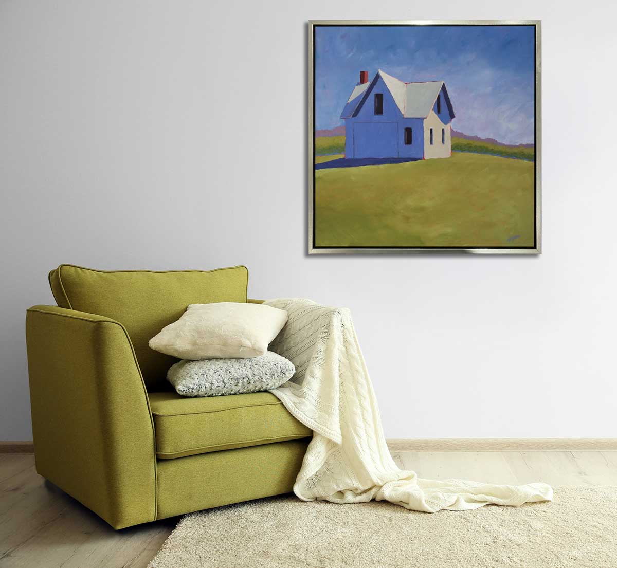 A blue and green contemporary barn print in a silver floater frame hangs on a white wall above a chartruse oversized chair with a white pillow, a textured white pillow and a white throw blanket.