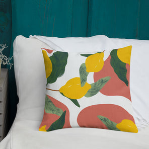 A medium size square pillow with a print of lemons on branches with terracotta and white organic shapes by Hazal Ozturk on a white couch. .