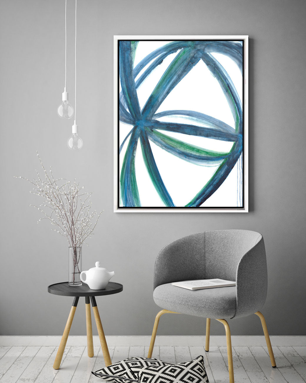 A blue, green, and white abstract print hangs on a grey wall above a modern grey armchair and a small wooden end table. 