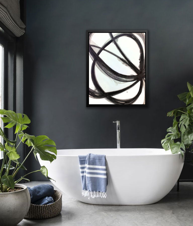 A black and white framed abstract print hangs on a dark wall above a modern bathtub and floor plants. 