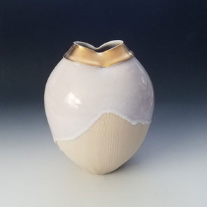 A textured off-white ceramic sculptural vessel with a white dripped glaze and a gold mouth, sitting on a grey gradient surface. 