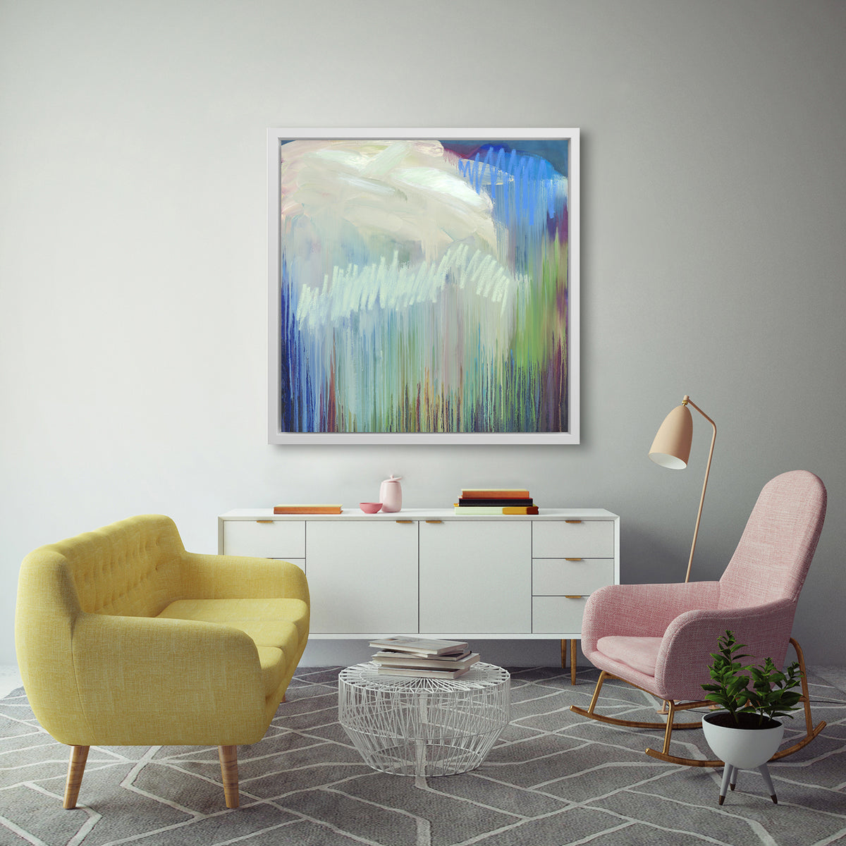 A multicolored abstract print in a white floater frame hangs on a white wall above a white dresser, a yellow sofa, a pink rocking chair and a white wire coffee table.