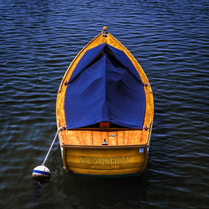 A photograph of a yellow-toned wooden row boat with a blue cover rests anchored in blue water. 