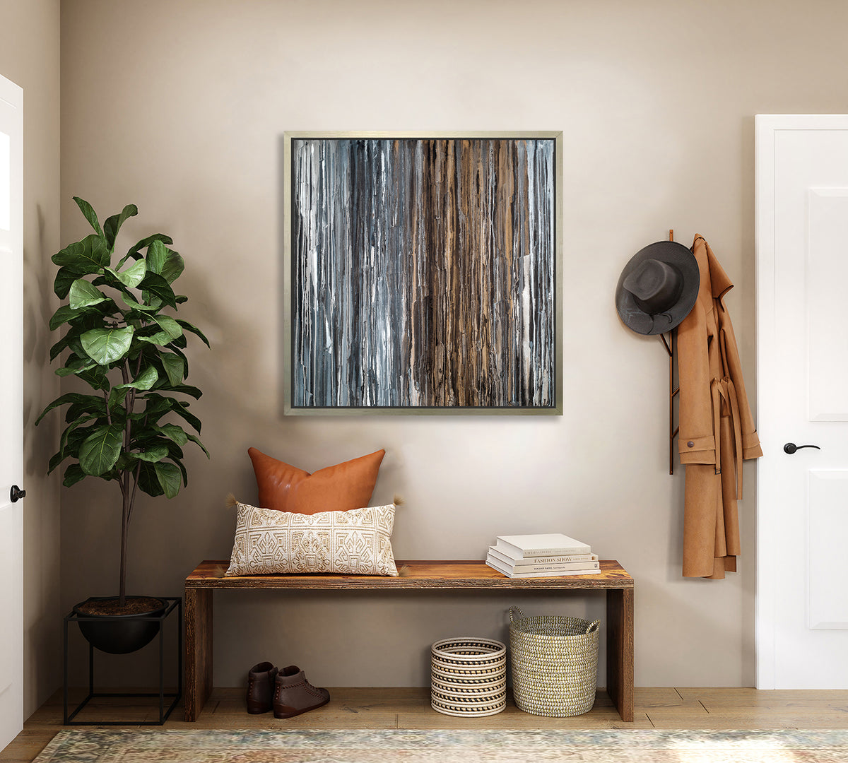 A brown, copper, white, grey and black abstract print in a silver floater frame hangs on a beige wall above a wood bench with pillows and books, a potted floor plant and a two woven baskets.