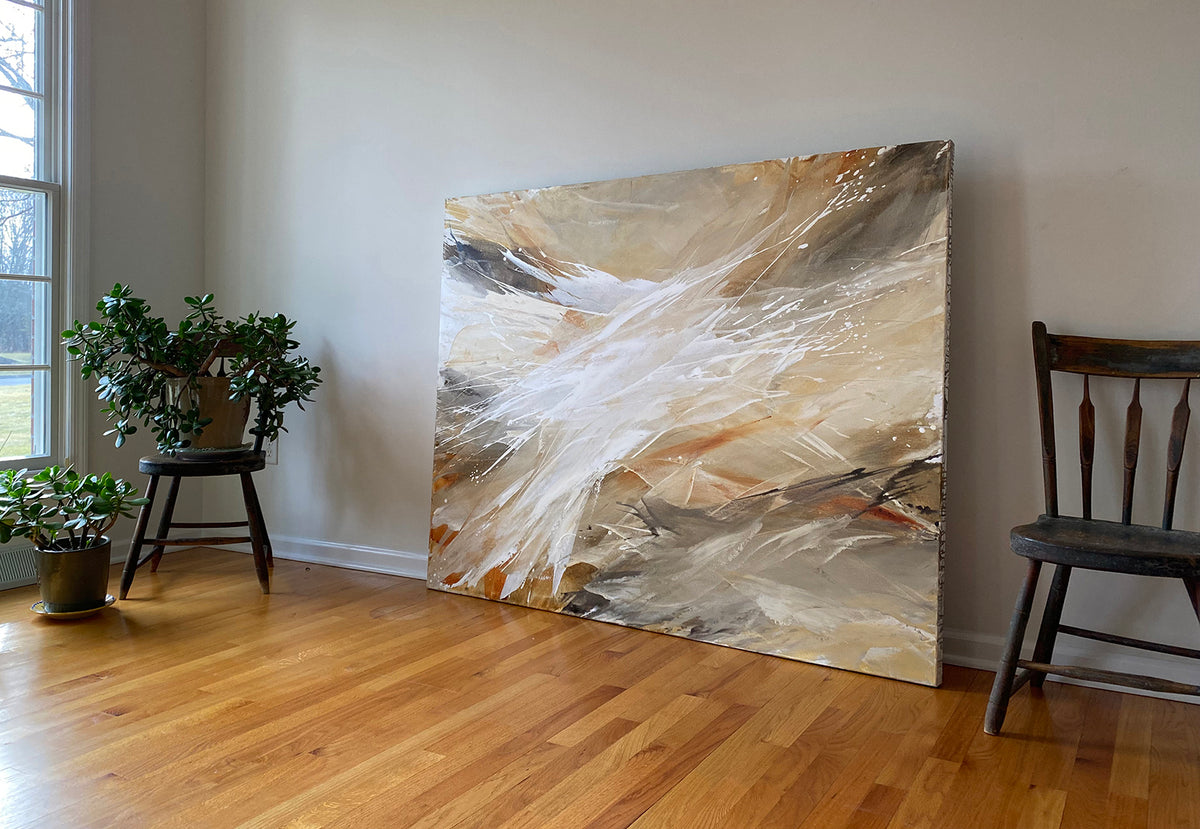 An orange, white, and brown abstract painting by Teodora Guererra sits on a hardwood floor with a brown wood chair below to the right. Also to the left a there is a window and plants sit on a chair and floor. 