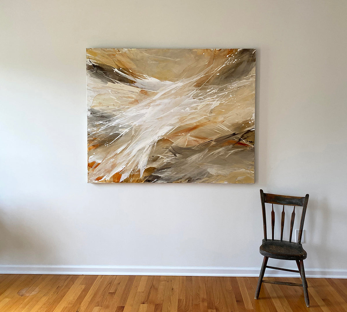 An orange, white, and brown abstract painting by Teodora Guererra hangs on a white wall with a brown wood chair below to the right.