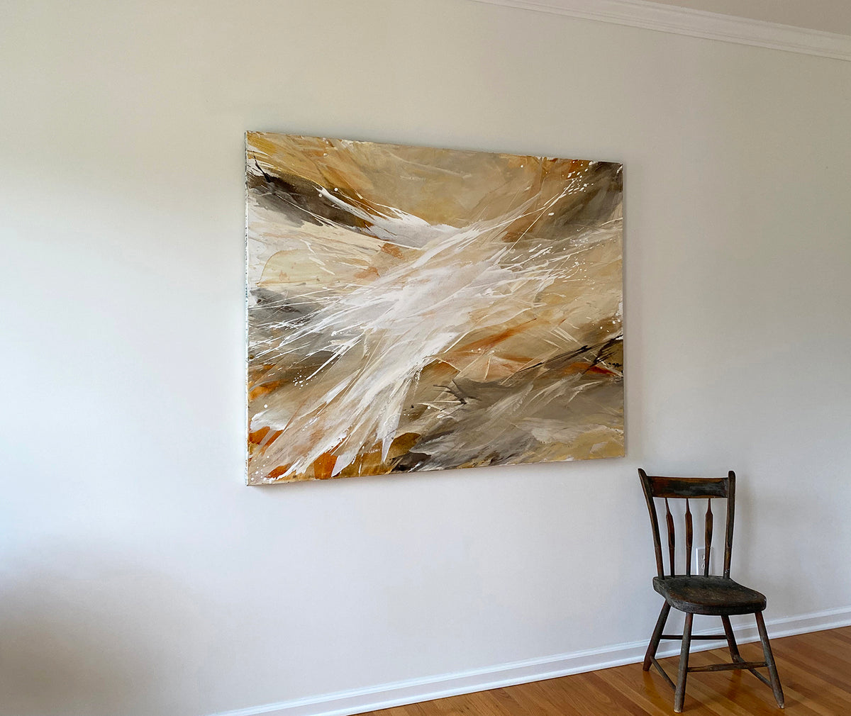 An orange, white, and brown abstract painting by Teodora Guererra hangs on a white wall with a brown wood chair below to the right.